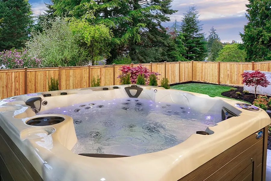 A hot tub in a fenced family backyard with lawn, flower beds and garden furniture