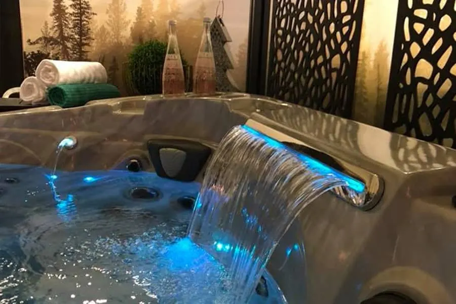 A close view of a lit waterfall feature running into a hot tub