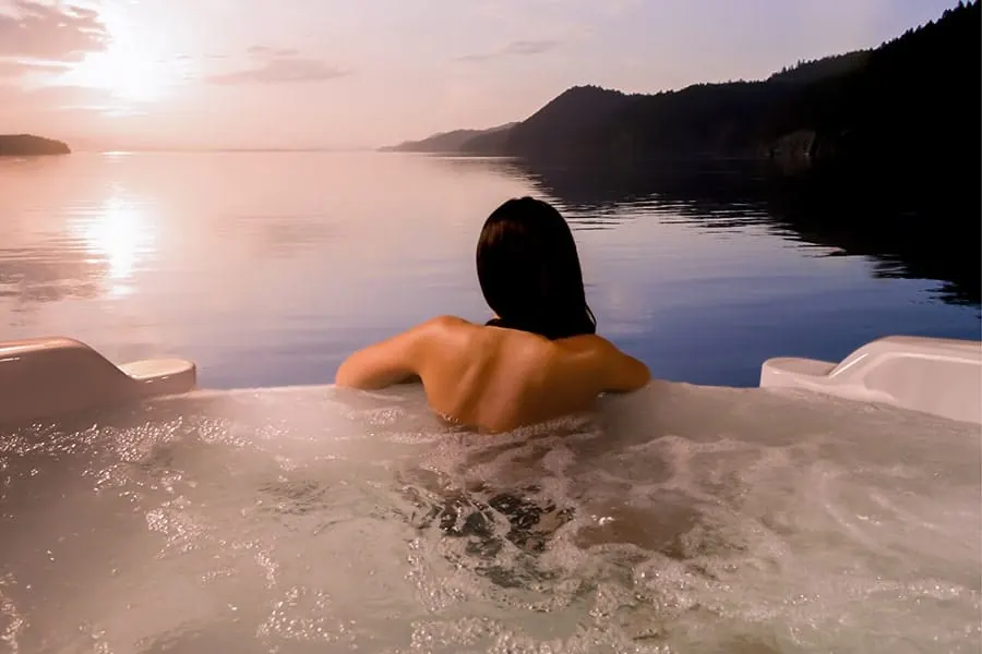One person sitting in a hot tub looking out over still water at sunset