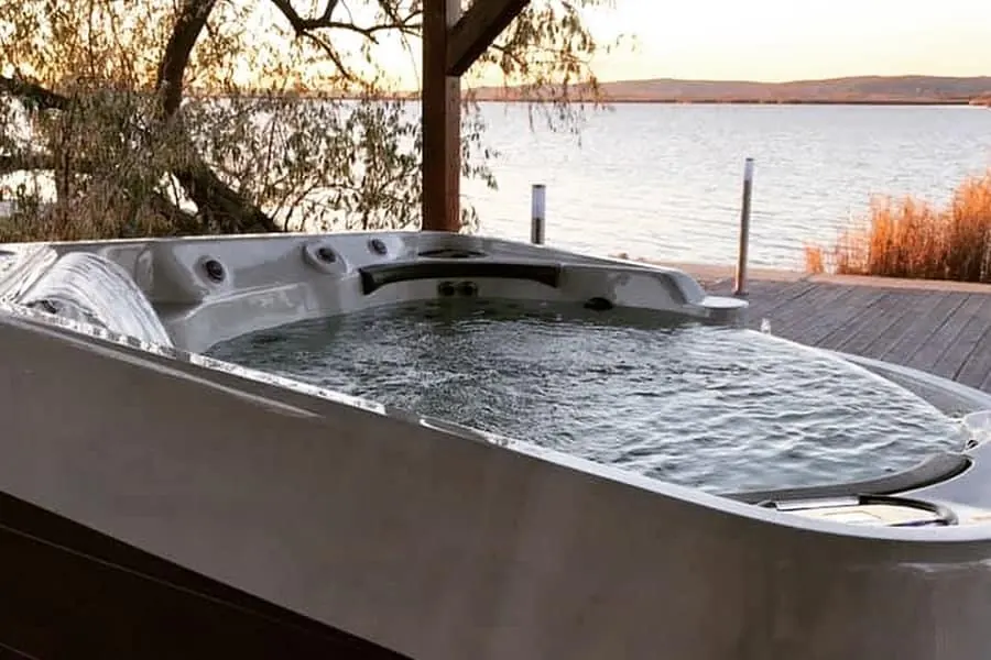 A swim spa on a deck beside open water with hills in the distance