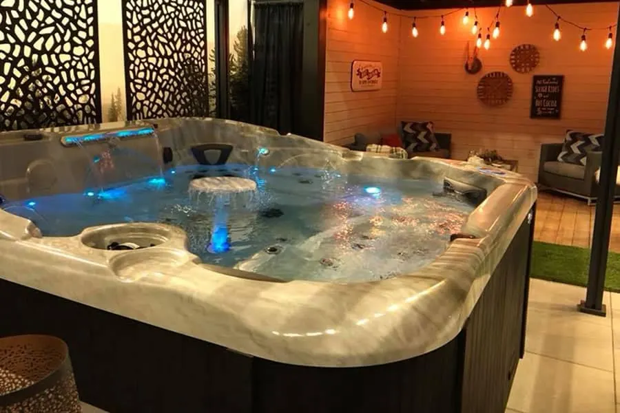 A large hot tub lit from within on a patio strung with festoon lights