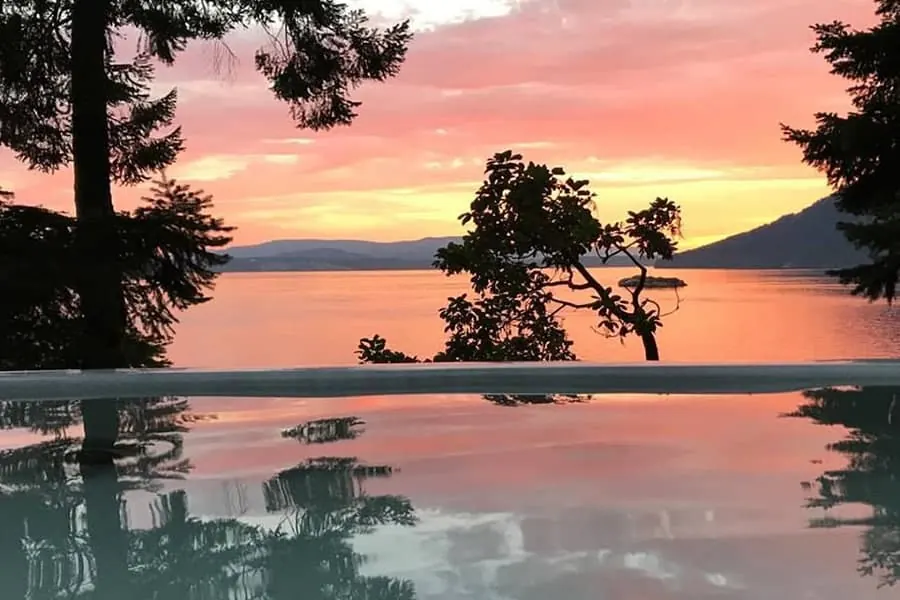 Warm water in the foreground with open sky and a distant treeline at sunset