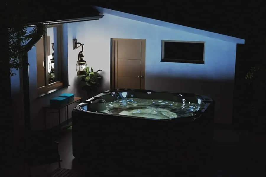 A compact hot tub tucked into a narrow side yard beside a house wall